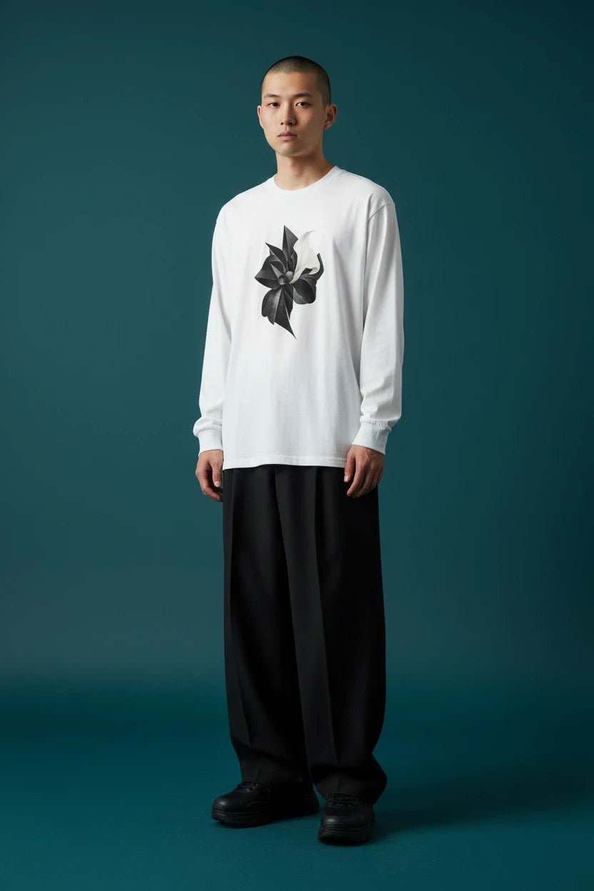 ODD COMMON white long-sleeve t-shirt featuring a black organic floral graphic, worn by a man with wide black trousers.
